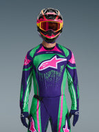 Alpinestars 2026 Techstar Nomur udstyrssæt, motocross-kører iført livlig grøn og lilla racingtrøje med pink detaljer, matchende udstyr med flerfarvet hjelm og goggles, højtydende off-road motorcykeloutfit