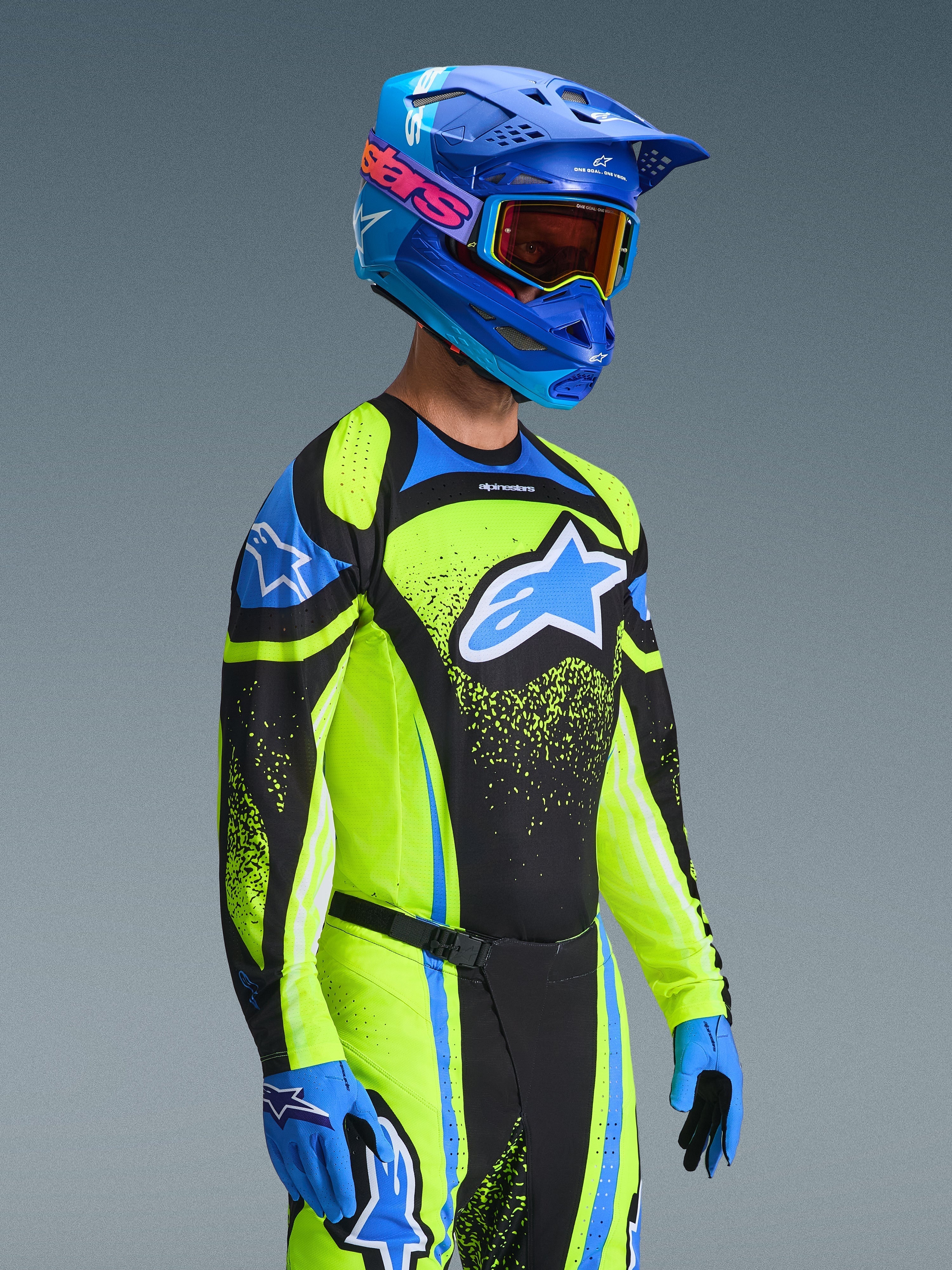 Motocrosskører iført Alpinestars 2026 Techstar Nomur-udstyrssæt, neongul og blå trøje med sorte paneler, stort blåt og hvidt logo på brystet, matchende blå hjelm med orange goggles, blå og sorte handsker, koordineret højtydende udstyr til off-road racing