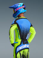 Alpinestars 2026 Techstar Nomur-trøje, motocross-kører set bagfra, neon gul og blå, atletisk race fit og fugttransporterende materiale, matchende bukser og blå hjelm, professionelt off-road racerudstyr
