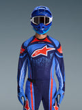 Motocross-kører iført Alpinestars 2026 Techstar Nomur trøje i Dark Navy, Orange og UCLA Blue, matchende bukser og blå handsker, blå hjelm med hvide crossbriller, stort rødt og hvidt Alpinestars-logo på brystet, koordineret high-performance gear til terrænkørsel.