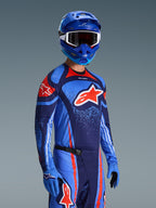 Motocross-kører iført Alpinestars 2026 Techstar Nomur-trøje, racingudstyr i Dark Navy, orange og UCLA Blue, med et stort orange Astars-logo, matchende blå hjelm og handsker, atletisk off-road konkurrencesæt.