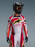Alpinestars 2026 Techstar Nomur trøje, motocross-trøje, rød, hvid og sort, med et stort sort A-star-logo på brystet med gule detaljer, rødt splatter-design, vist med en sort hjelm og matchende off-road-udstyr