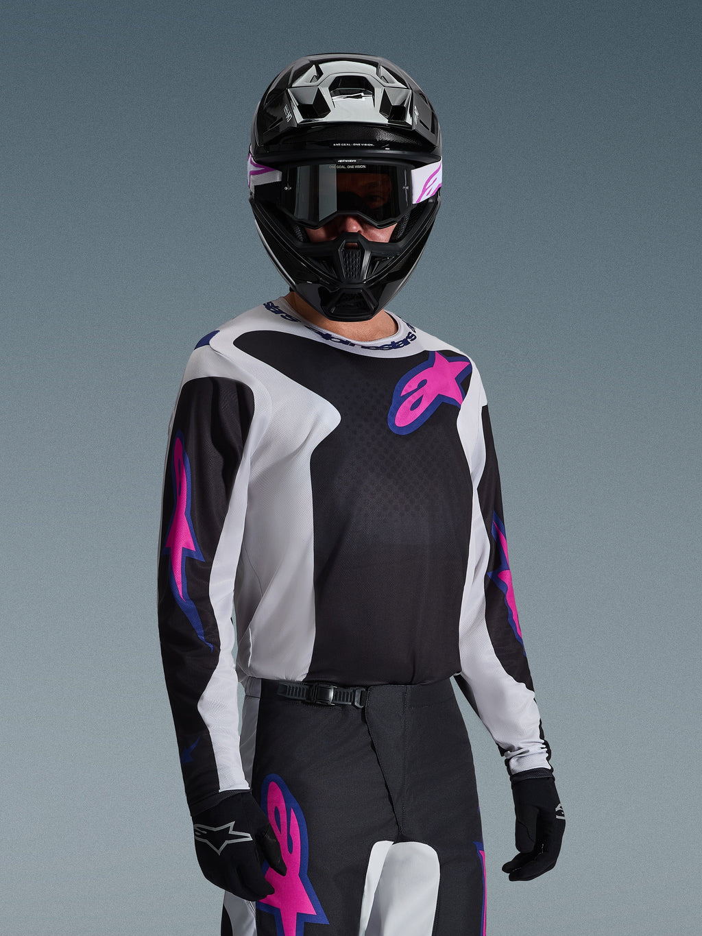 Motocrosskører iført Alpinestars 2026 Fluid Grid Jersey, sort, lysegrå og lilla, med store lyserøde og lilla stjernelogoer, kombineret med matchende bukser, sort hjelm og goggles, komplet sæt off-road racerudstyr