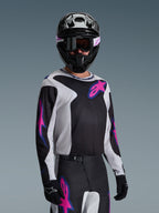 Motocrosskører iført Alpinestars 2026 Fluid Grid Jersey, sort, lysegrå og lilla, med store lyserøde og lilla stjernelogoer, kombineret med matchende bukser, sort hjelm og goggles, komplet sæt off-road racerudstyr