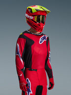 Alpinestars 2026 Fluid Grid-udstyrssæt, motocrosskører iført rød og sort jersey med hvide og blå logodetaljer, matchende røde og sorte bukser, rød hjelm med gule highlights og guld-goggles, koordineret off-road racingudstyr