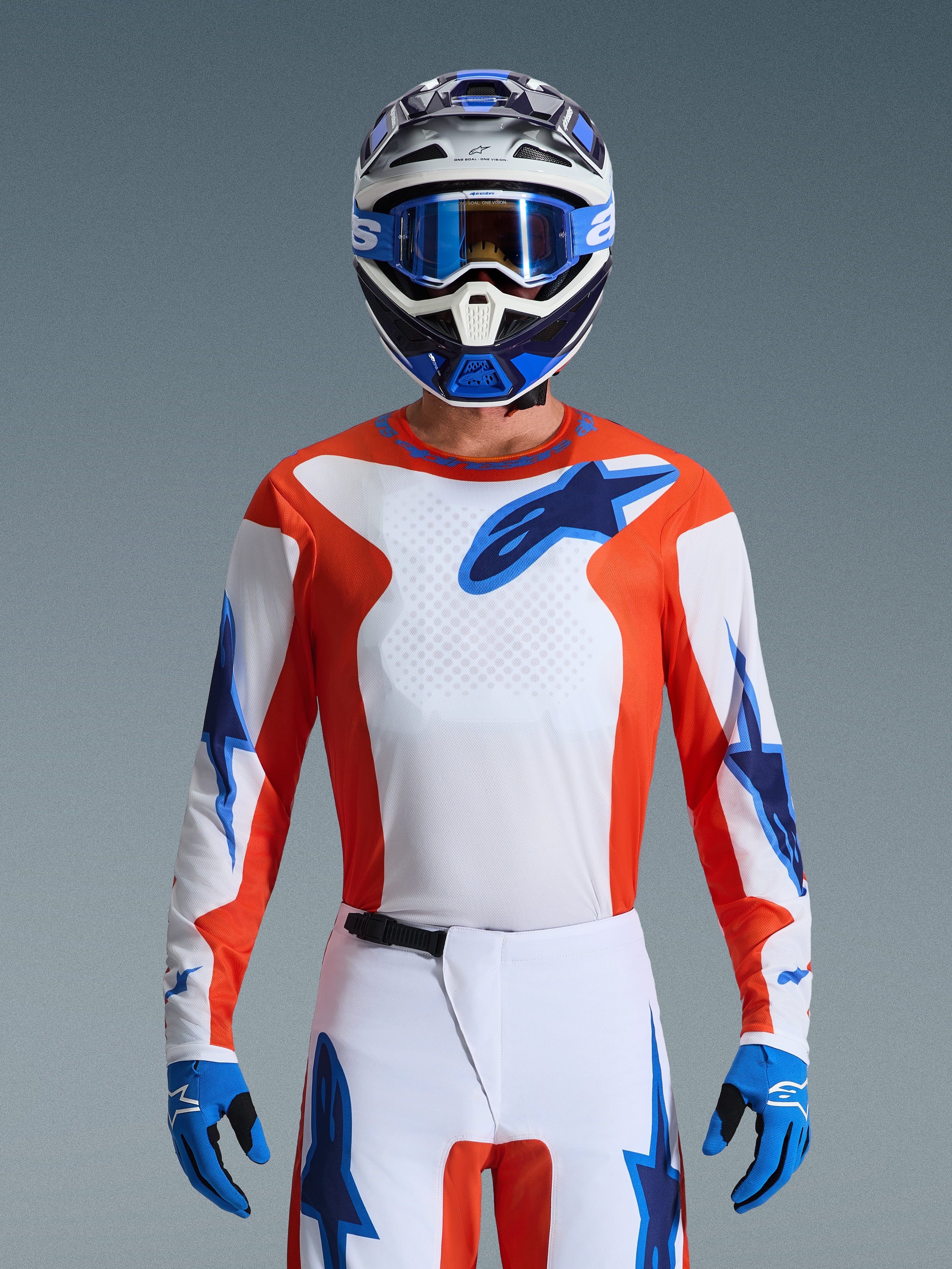 Alpinestars 2026 Fluid Grid Gear Set, motocross-kører iført orange og hvid trøje med blå stjernelogoer, hvide bukser med blå detaljer, matchende blå og hvid hjelm med blå briller og handsker, komplet off-road racingudstyr