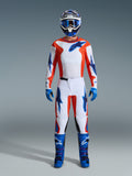 Alpinestars 2026 Fluid Grid udstyrssæt, motocross-rytter i fuldt udstyr, hvid trøje og bukser med orange og UCLA blå detaljer, matchende blå og hvid hjelm med blå motocross-briller, blå handsker og blå motocross-støvler, koordineret raceroutfit til terrænkørsel
