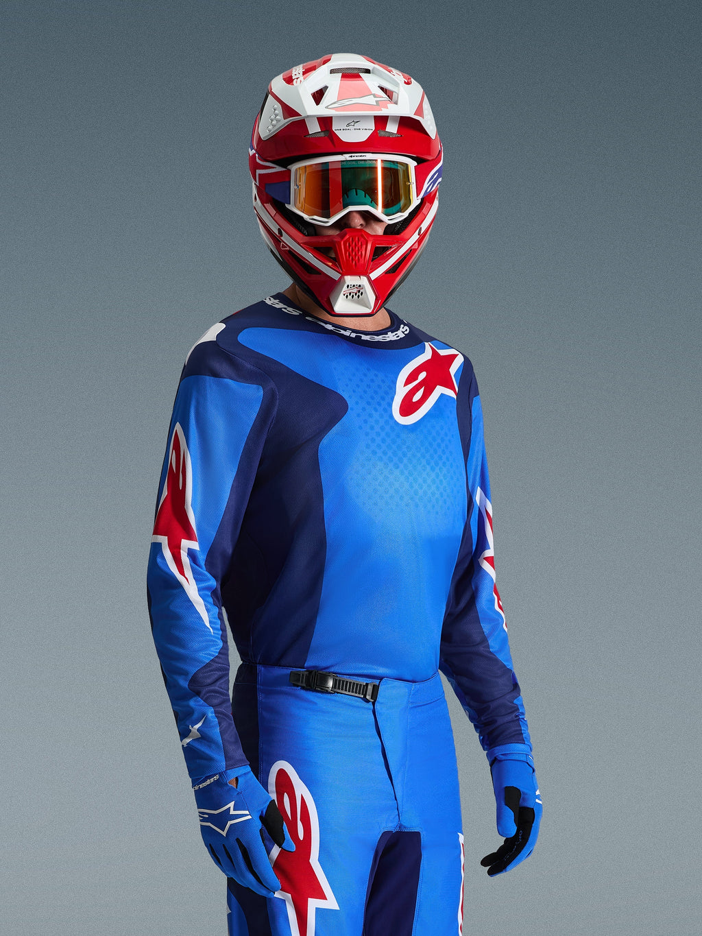 Motocross-kører iført Alpinestars 2026 Fluid Grid-trøje i blå og rød, med røde Alpinestars-stjernelogoer, kombineret med matchende blå bukser, blå handsker og en rød og hvid hjelm med goggles