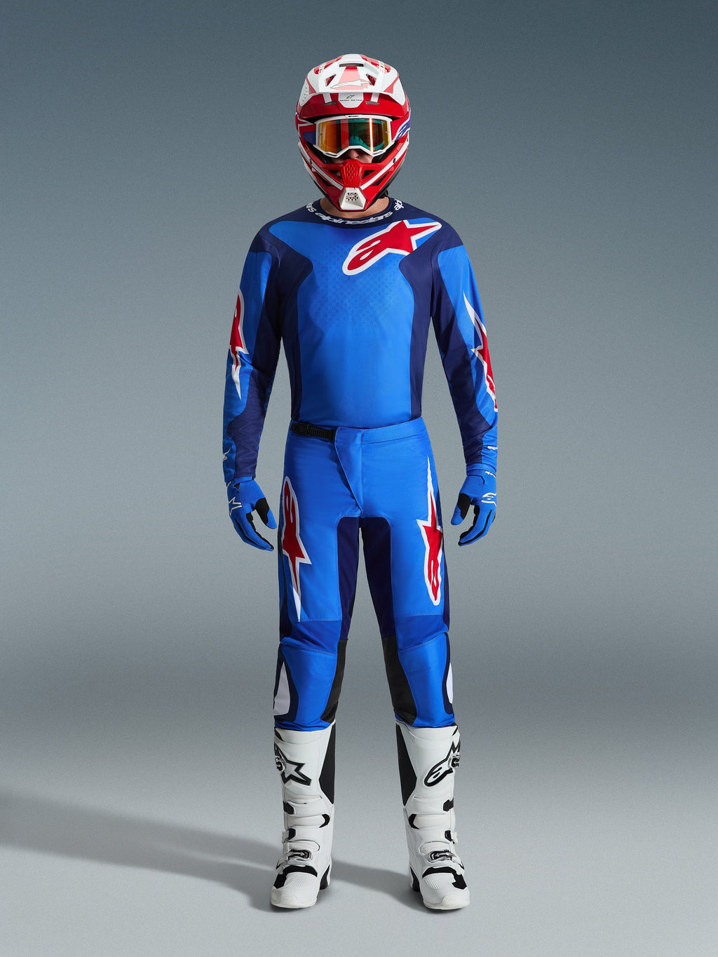 Motocross-kører iført Alpinestars 2026 Fluid Grid jersey i blå og rød, matchende blå bukser med hvide og røde stjernelogoer, rød og hvid hjelm med spejlglas-goggles, blå handsker og hvide og sorte racingstøvler, komplet off-road udstyrssæt