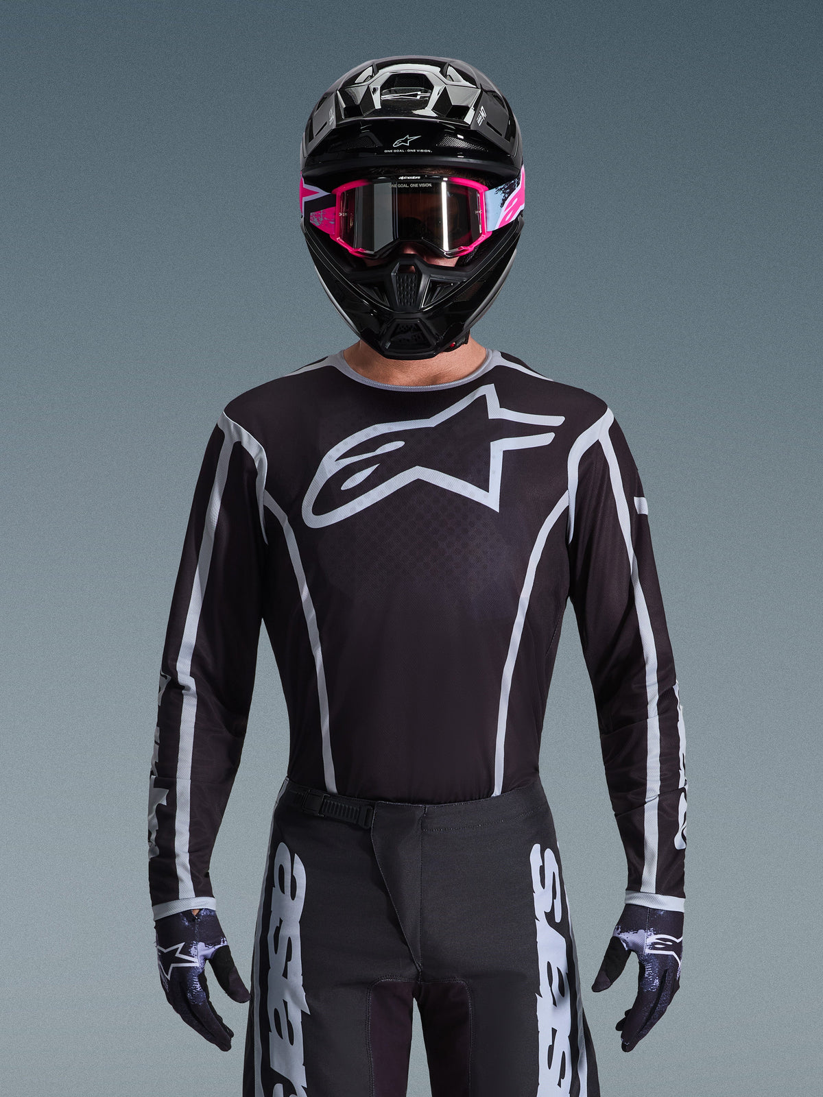 Alpinestars 2026 Fluid Apex trøje, motocross-trøje, sort og grå, med et stort hvidt Astars-logo på brystet og grå grafiske detaljer på ærmerne, båret af en kører med lyserøde goggles og en sort hjelm, koordineret off-road-racerudstyr