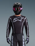 Alpinestars 2026 Fluid Apex trøje, motocross-trøje, sort og grå, med et stort hvidt Astars-logo på brystet og grå grafiske detaljer på ærmerne, båret af en kører med lyserøde goggles og en sort hjelm, koordineret off-road-racerudstyr