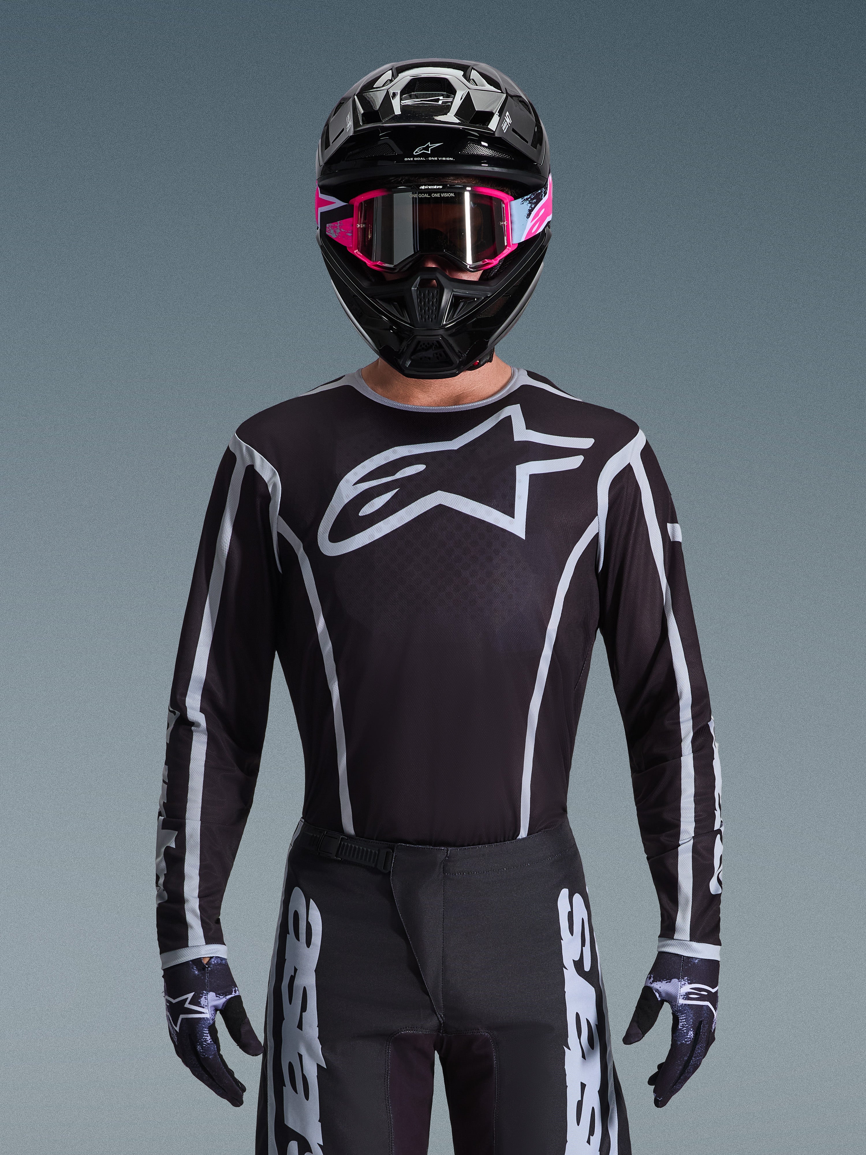 Alpinestars 2026 Fluid Apex trøje, motocross-trøje, sort og grå, med et stort hvidt Astars-logo på brystet og grå grafiske detaljer på ærmerne, båret af en kører med lyserøde goggles og en sort hjelm, koordineret off-road-racerudstyr