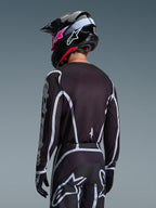Motocross-kører set bagfra iført Alpinestars 2026 Fluid Apex trøje i sort og grå, matchende motocross-bukser med hvide detaljer, sort hjelm med pink branding, koordineret outfit til off-road kørsel