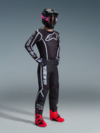 Motocross-kører iført 2026 Fluid Apex trøje, sort og grå, matchende bukser, sort hjelm med lyserøde goggles og knaldrøde støvler, markant hvidt Alpinestars-branding på bryst og ærmer, koordineret professionelt off-road raceroutfit.
