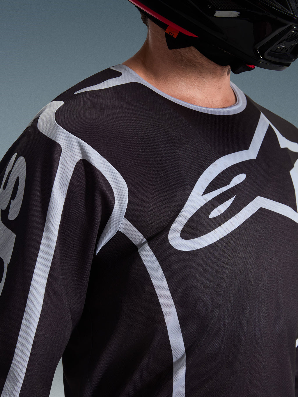 Alpinestars 2026 Fluid Apex jersey, motocross-trøje, sort og grå, med stort Alpinestars-logo på brystet, sportskrave, båret med en sort hjelm, performance-udstyr til terrænkørsel