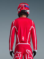 Alpinestars 2026 Fluid Apex-trøje, rød og hvid, set bagfra på en motocross-kører, geometriske hvide mønstre, matchende motocross-bukser og rød hjelm, komplet racerudstyr til off-road-kørsel.
