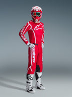Motocross-kører iført Alpinestars 2026 Fluid Apex-udstyrssæt, rød trøje med store hvide logoer, matchende røde bukser med hvid branding, hvid og rød hjelm, hvide motocross-støvler og -handsker, koordineret outfit til off-road-kørsel