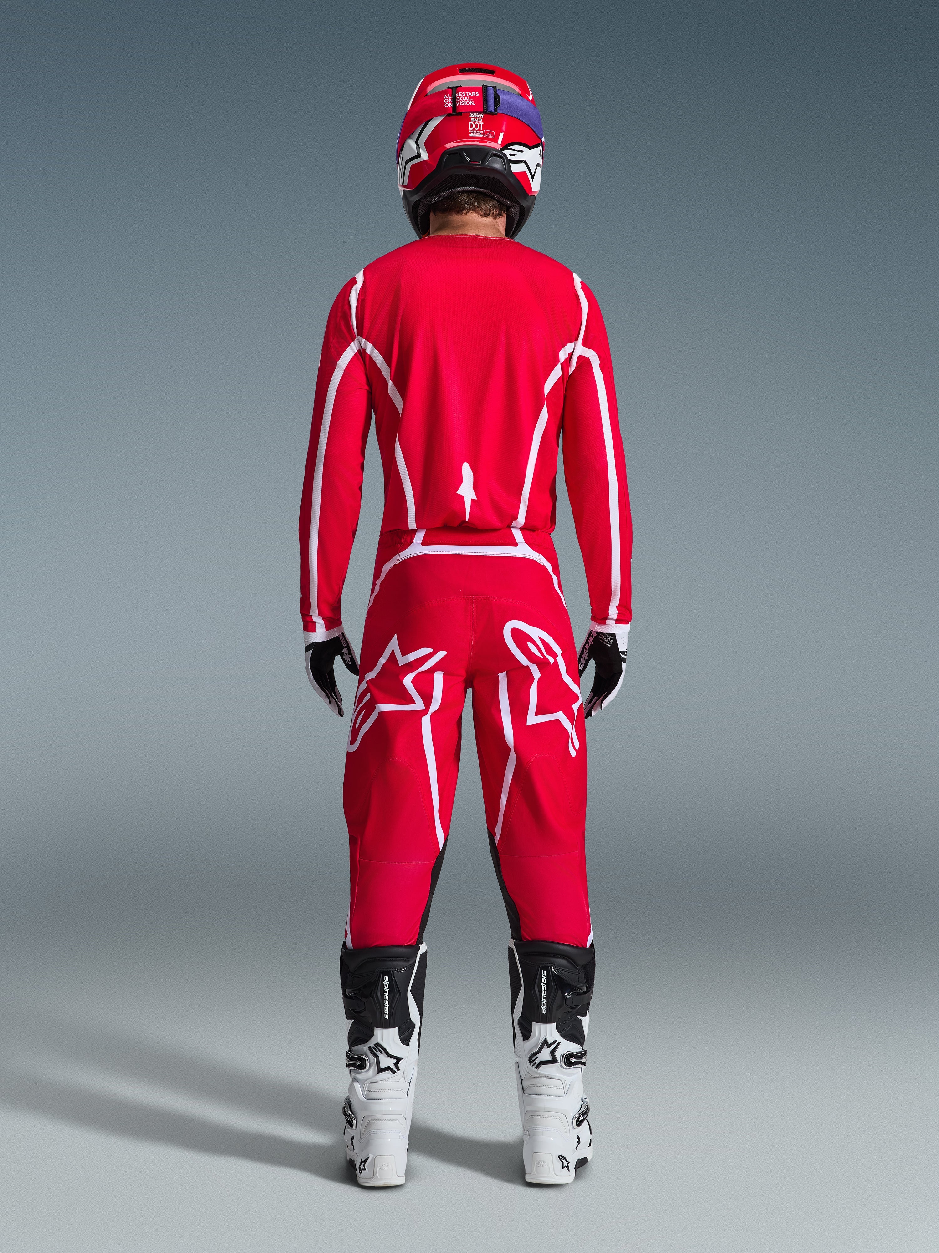 Bagfra af en motocrosskører iført Alpinestars 2026 Fluid Apex-udstyrssæt, klar rød trøje og bukser med hvide striber og logoer, kombineret med hvide og sorte støvler og en rød hjelm, professionelt off-road racerudstyr