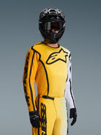 Motocross-kører iført Alpinestars 2026 Fluid Apex-udstyrssæt, gul og hvid jersey med sort stjernelogo og detaljer, matchende gule bukser, sort hjelm med sorte goggles og sorte handsker, koordineret outfit til terrænkørsel