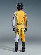 Motocross-kører set bagfra iført Alpinestars 2026 Fluid Apex Jersey og matchende bukser i gul og sort, med markante farveblokerede paneler i hvid, gul og orange, kombineret med sort hjelm og motocross-støvler.