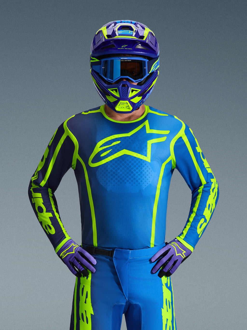 Motocross-kører iført Alpinestars 2026 Fluid Apex Jersey i Blue Yellow Fluo, med en klar blå base, fluorescerende gul grafik og et stort brystlogo, koordineret med matchende hjelm og handsker, designet til terrænkørsel og motocross.