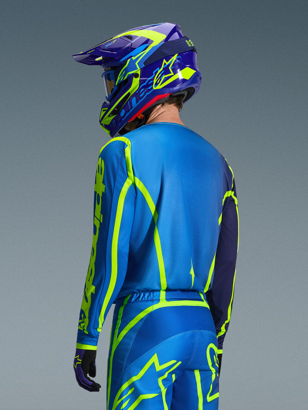 Alpinestars 2026 Fluid Apex trøje, Blue Yellow Fluo, set bagfra af kører iført matchende motocrossbukser og hjelm, med fluorescerende gul geometrisk grafik og en afslappet atletisk pasform, koordineret off-road racerudstyr