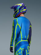 Alpinestars 2026 Fluid Apex trøje, Blue Yellow Fluo, set bagfra af kører iført matchende motocrossbukser og hjelm, med fluorescerende gul geometrisk grafik og en afslappet atletisk pasform, koordineret off-road racerudstyr