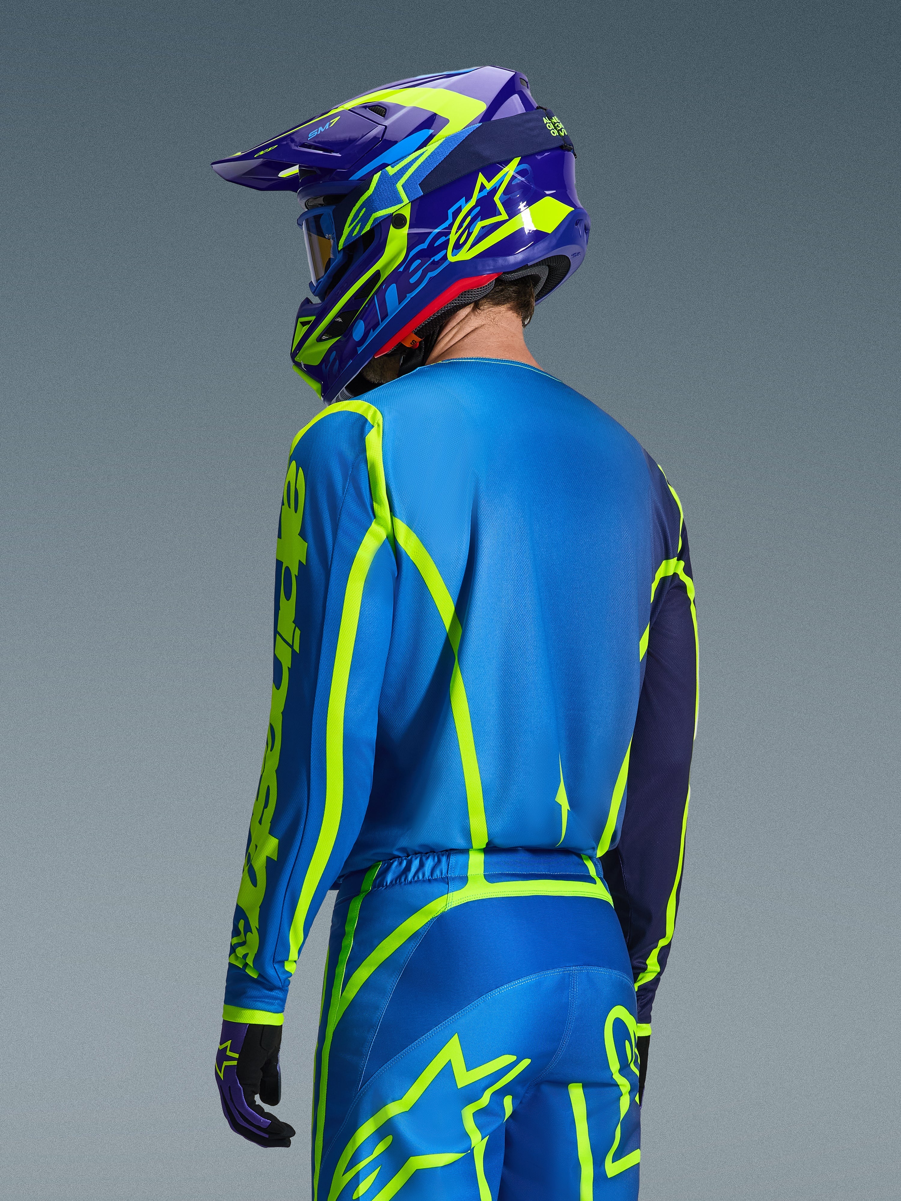 Alpinestars 2026 Fluid Apex trøje, Blue Yellow Fluo, set bagfra af kører iført matchende motocrossbukser og hjelm, med fluorescerende gul geometrisk grafik og en afslappet atletisk pasform, koordineret off-road racerudstyr