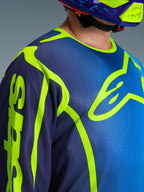 Alpinestars 2026 Fluid Apex trøje, motocross-trøje i blå og gul fluo, nærbillede der viser det store neongule brystlogo og branding på ærmet, åndbar polyfabric-konstruktion med ergonomisk sportskrave