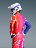 Motocross-kører set bagfra iført Alpinestars 2026 Fluid Apex Jersey, flerfarvet rød, pink og lilla gradient med hvide grafiske detaljer, matchende bukser, hvid hjelm med blå briller, sort-hvide handsker, koordineret off-road udstyr
