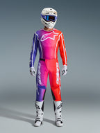 Motocross-kører iført et komplet Alpinestars 2026 Fluid Apex racersæt, med trøje og bukser i en lilla, lyserød og orange gradient. Det matchende sæt inkluderer et hvidt Alpinestars-logo på brystet, en hvid hjelm med blå goggles og hvide støvler, designet til off-road præstationer.