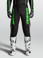 Alpinestars Fluid Apex V2 bukser, motocross-bukser i grøn og sort, forstærkede knæ og polyfabric-konstruktion, båret med hvide støvler, avanceret off-road ydeevne.