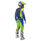 Alpinestars 2024 Racer Hoen Jersey i Yellow Fluo og Blue Night Navy, motocrosskører set bagfra med matchende bukser og hvide støvler, viser det bageste design med røde logoer, koordineret outfit til professionel terrænkørsel