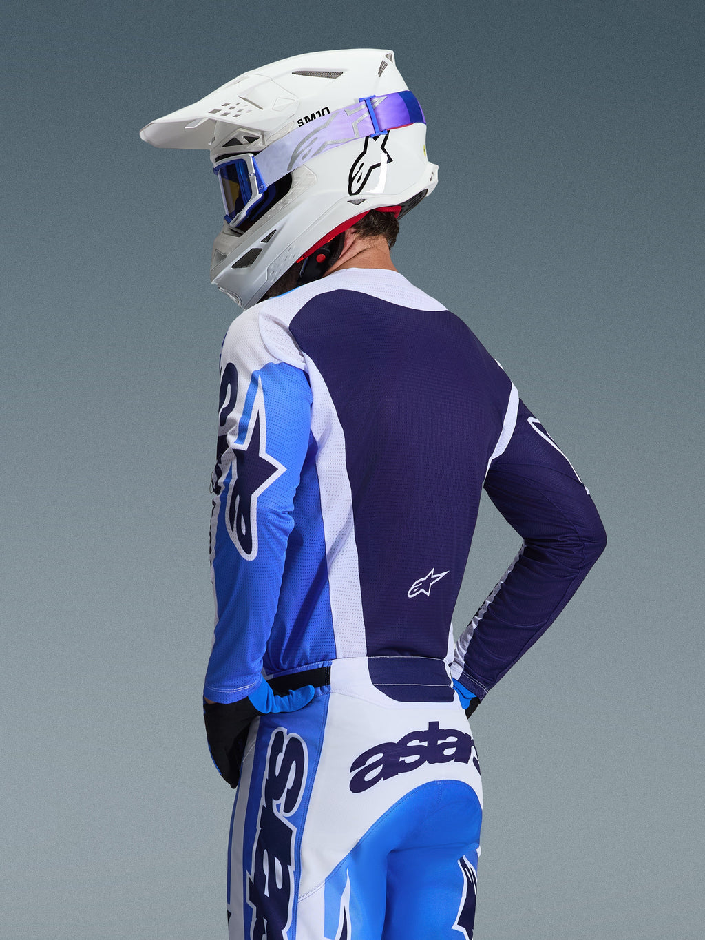 Motocrosskører iført Alpinestars 2026 Racer Air Portl trøje i Ucla Blue og hvid, set bagfra med fokus på det åndbare mørkeblå mesh-rygpanel, båret med matchende bukser og en hvid Alpinestars-hjelm med blå briller, koordineret motocross-udstyrssæt.