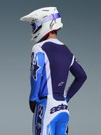 Motocrosskører iført Alpinestars 2026 Racer Air Portl trøje i Ucla Blue og hvid, set bagfra med fokus på det åndbare mørkeblå mesh-rygpanel, båret med matchende bukser og en hvid Alpinestars-hjelm med blå briller, koordineret motocross-udstyrssæt.