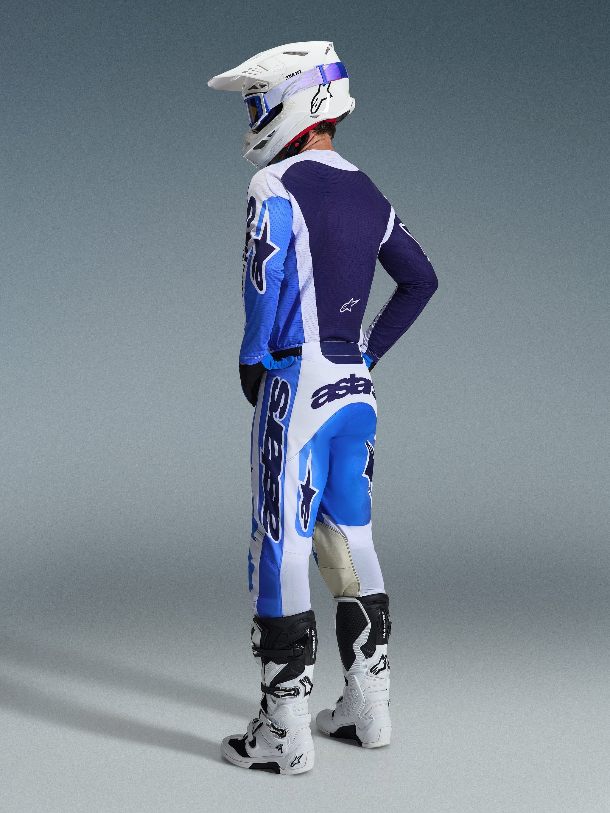 Motocrossrytter set bagfra iført Alpinestars 2026 Racer Air Portl trøje i Ucla Blue og hvid, matchende motocrossbukser, hvid Supertech hjelm og hvide støvler, der viser et komplet koordineret racersæt.