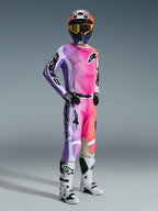 Alpinestars 2026 Racer Air Portl bukser, motocross-kører iført komplet racerudstyr, lyserødt, lilla og orange flerfarvet design med hvide detaljer, matchende langærmet trøje, sort hjelm med gule goggles og hvide støvler, professionelt udstyr til terrænkørsel