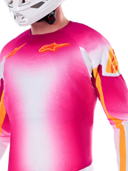 Alpinestars Limited Edition Supertech AFD MIG Jersey, motocross-jersey i pink fluo og hvid gradient, med orange Astars-logoer og ærmedetaljer, båret af en kører med hvid hjelm, atletisk racerpasform.