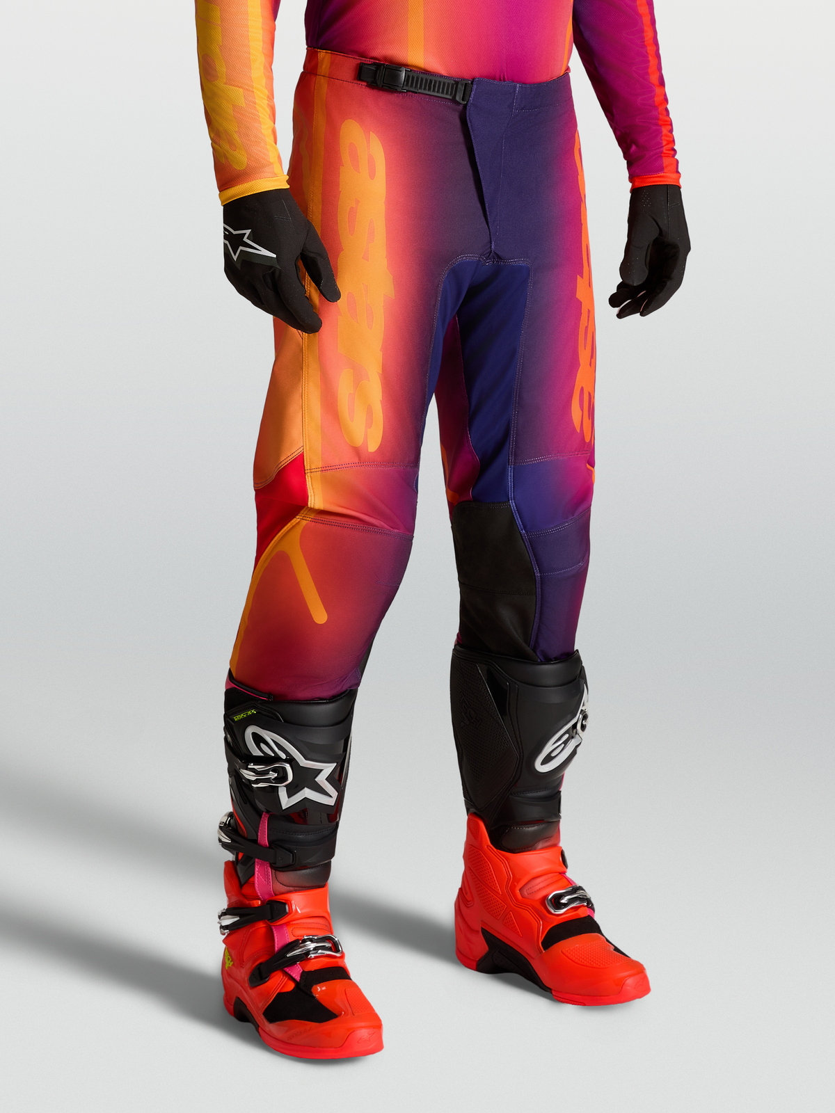 Alpinestars Fluid Kepler bukser, off-road motocross-bukser i lilla og orange, sport fit med forstærkede knæ og forbuet design, båret med Tech-støvler.