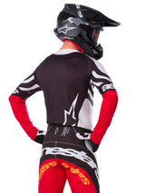 Motocrossrytter set bagfra iført Alpinestars Limited Edition Techstar Deep-trøje, sort, hvid og High Red, med matchende racerbukser og en sort hjelm, atletisk pasform til off-road-præstation