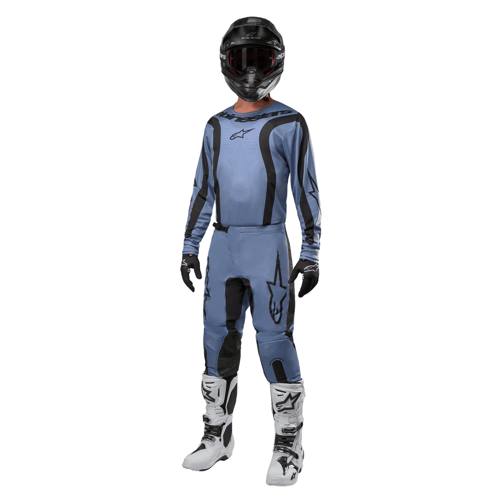 Motocross-kører iført komplet racerudstyr, Alpinestars 2024 Fluid Lurv-trøje i lyseblå og sort, matchende lyseblå bukser med sorte paneler, hvide og sorte støvler, sorte handsker og sort hjelm med goggles, koordineret sæt til terrænkørsel