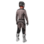 Alpinestars 2024 Fluid Lurv Jersey, Motocross Jersey, Mud Black, rear view of motocross rider wearing matching racing gear, black helmet, and white boots, featuring bold black Alpinestars logos and an athletic fit for off-road performance.