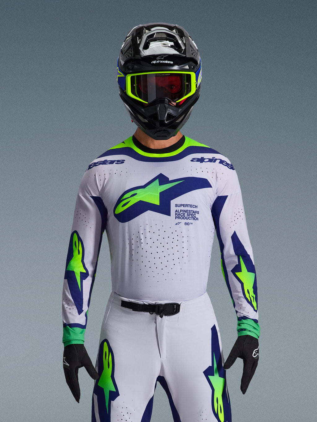 Alpinestars 2026 Supertech Vista trøje, motocross-jersey, lysegrå, neon-gul og blå, båret af en kører med matchende bukser og sort hjelm, med et stort brystlogo og laser-skårne perforeringer til ventilation, atletisk pasform på pro-niveau