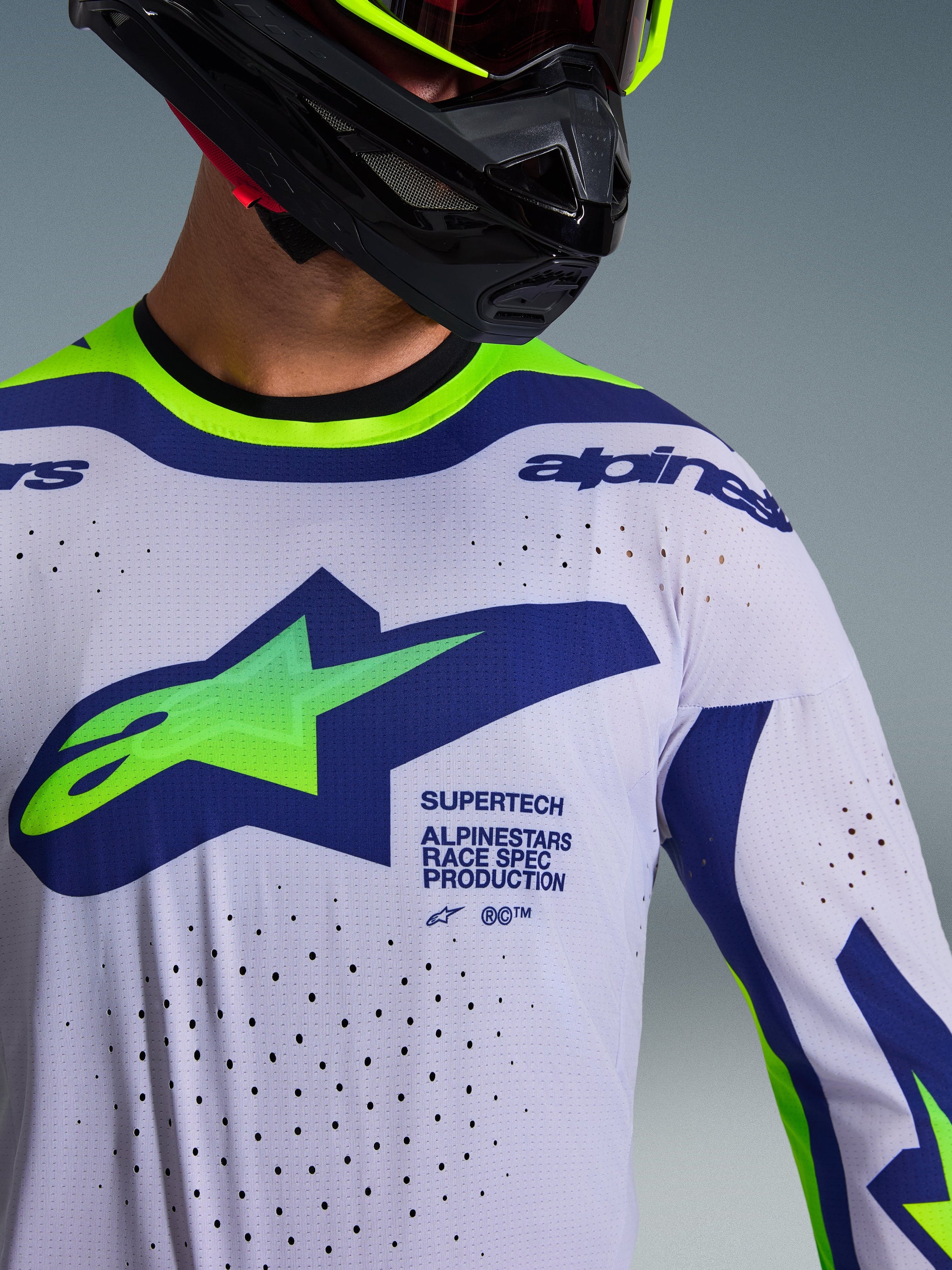 Alpinestars 2026 Supertech Vista Jersey, motocross-trøje, lysegrå med neongule og blå detaljer, båret af kører med sort hjelm og neongule goggles, har et stort grønt og blåt Astars-logo, laser-skårne ventilationshuller og atletisk race-fit design
