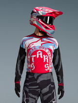 Alpinestars Techstar Beast Coast trøje i rød og blå med cirkulær grafik, matchende motocross-hjelm og camouflage-bukser.