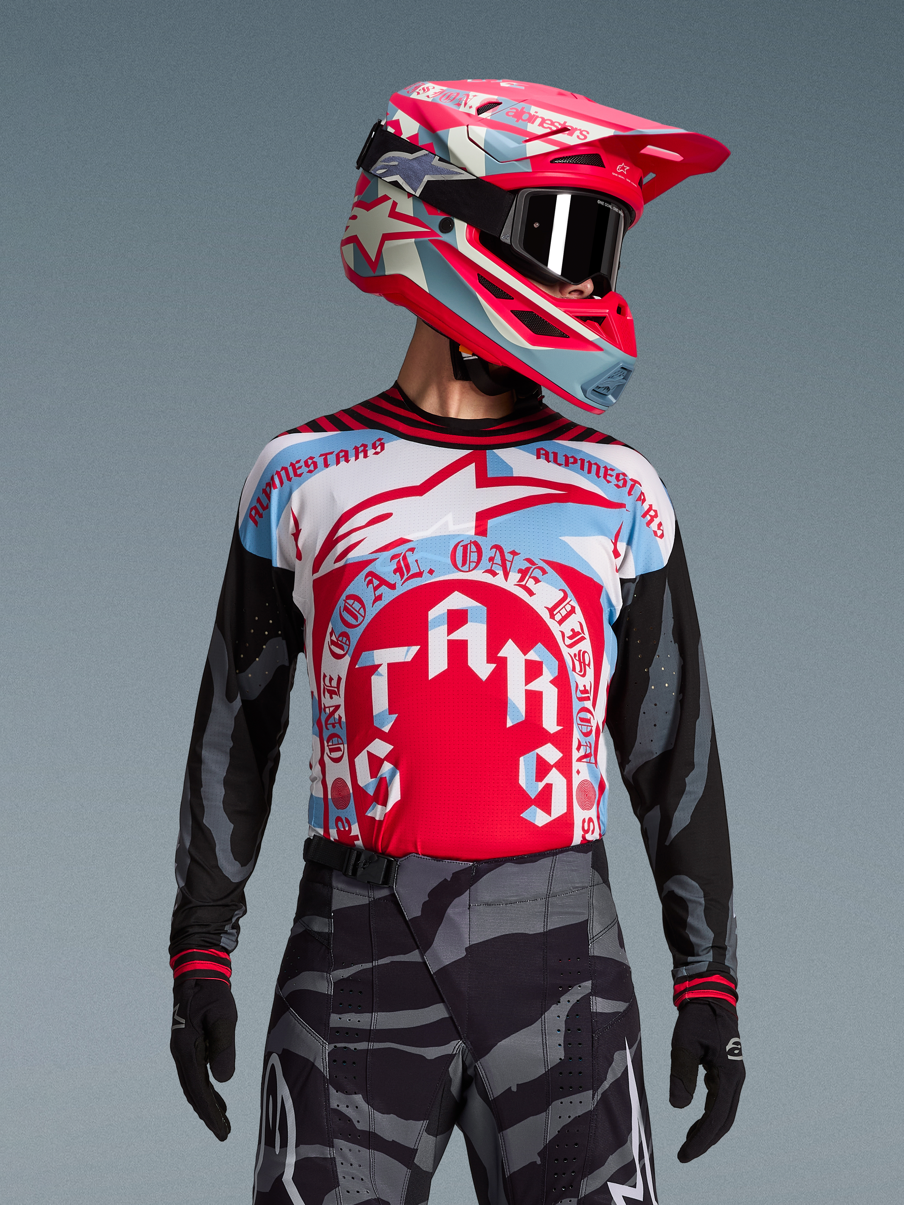 Alpinestars Techstar Beast Coast trøje i rød og blå med cirkulær grafik, matchende motocross-hjelm og camouflage-bukser.