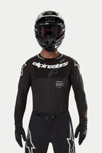 Motocross rider wearing the Alpinestars 2024 Supertech Ward Jersey in Black, athletic race fit with white Alpinestars logo on the chest, featuring laser-cut perforations and 'Supertech Race Spec' text, paired with a black helmet and goggles for off-road racing.