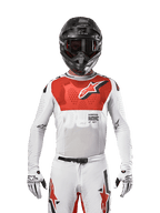 Motocrossrytter iført Alpinestars 2024 Supertech Ward Jersey i White Hot Orange, hvid mesh-trøje med stræk og en markant rød grafik og logo på brystet, sort hjelm med mørke goggles, hvide handsker, professionelt udstyr til terrænkørsel