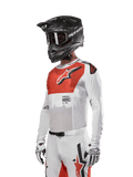 Alpinestars 2024 Supertech Ward Jersey, motocross-trøje, hvid og hot orange, med rødt brystpanel og hvidt stjernelogo, lange ærmer med laserskårne perforeringer, båret med sort hjelm og hvide handsker, atletisk race fit motocross-udstyr