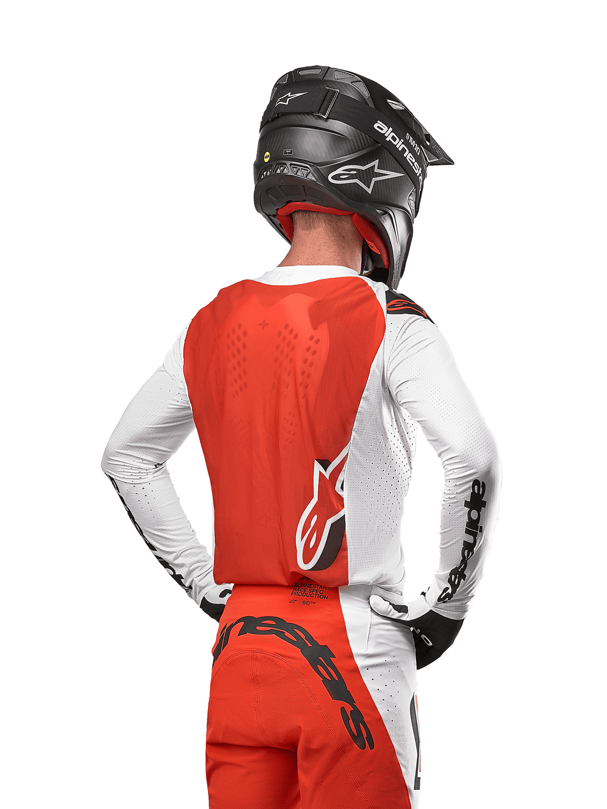 Motocross-rytter iført 2024 Supertech Ward Jersey i farven White Hot Orange, set bagfra, viser det orange rygpanel og de hvide ærmer med sort Alpinestars-branding, kombineret med matchende bukser og sort hjelm, professionelt udstyr til off-road racing